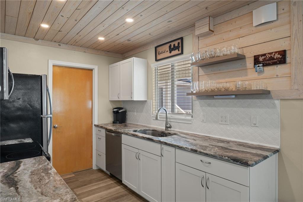 Kitchen with stainless steel appliances, backsplash, wood ceiling, white cabinets, and a sink