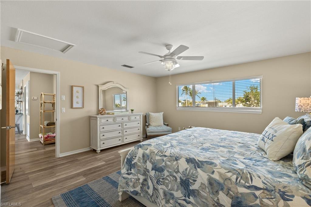 Bedroom with wood finished floors, visible vents, a ceiling fan, baseboards, and attic access