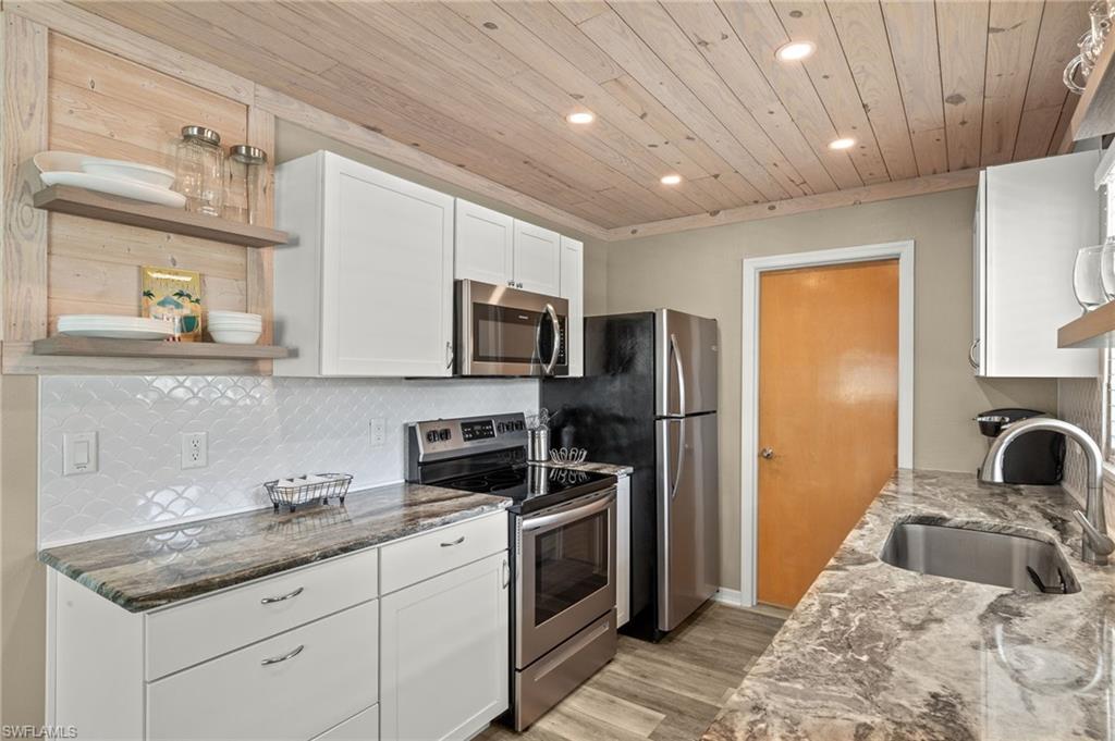 Kitchen featuring dark stone countertops, decorative backsplash, stainless steel appliances, and a sink