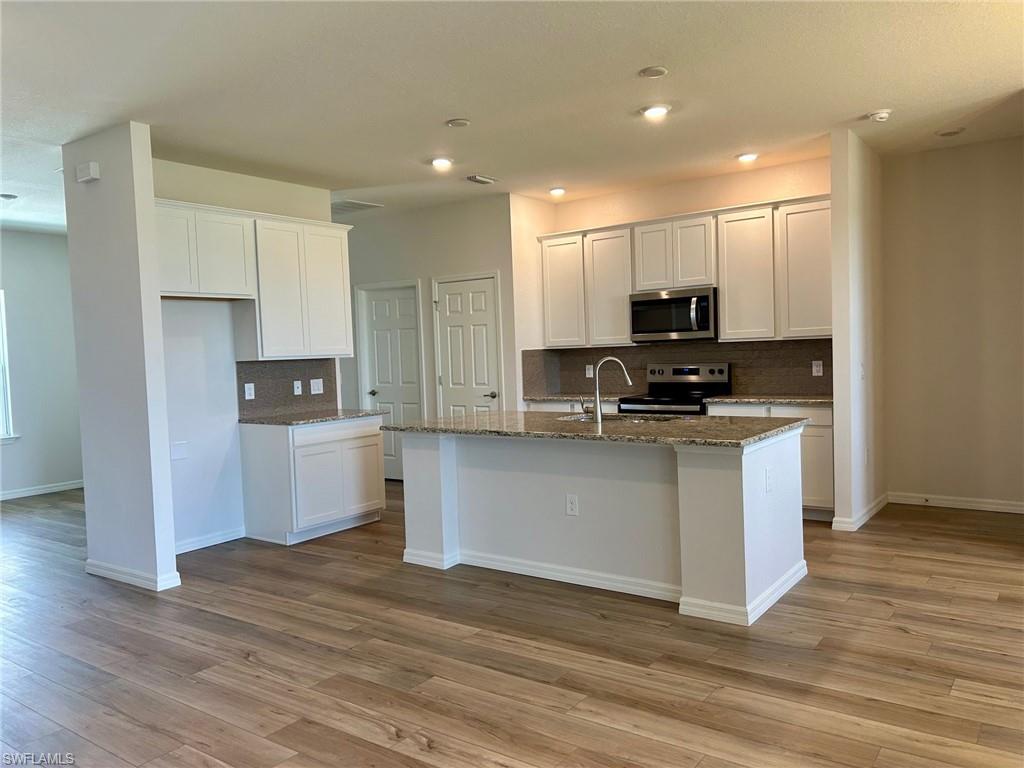 Kitchen with appliances with stainless steel finishes, backsplash, light wood-style floors, a kitchen island with sink, and dark stone counters