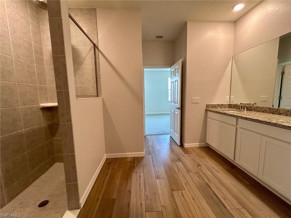 Bathroom with vanity, wood finished floors, a walk in shower, and baseboards