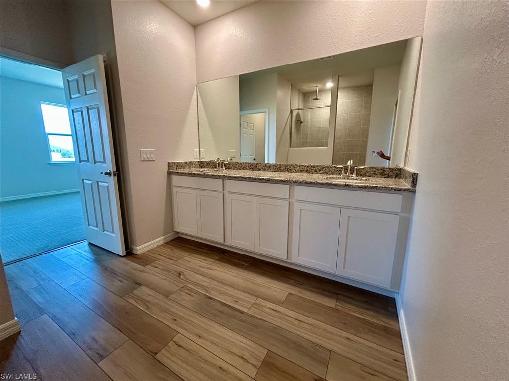 Full bathroom with a textured wall, double vanity, a tile shower, wood finished floors, and baseboards