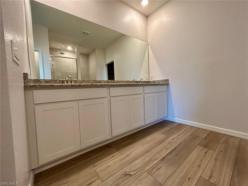 Bathroom with wood finished floors, double vanity, a tile shower, baseboards, and a textured wall