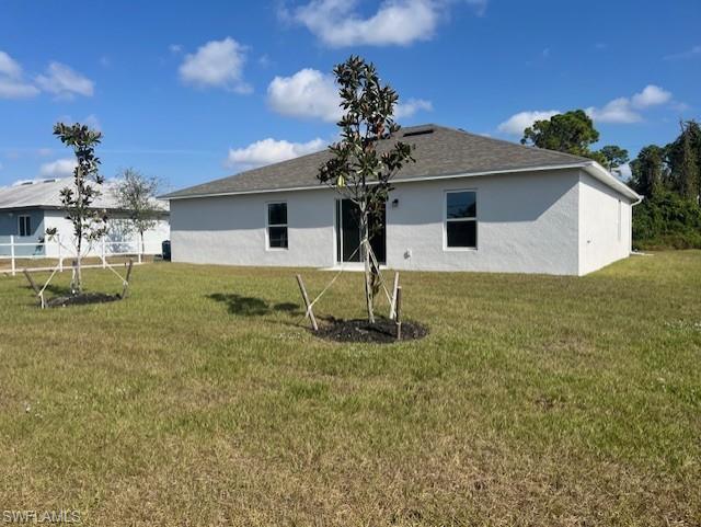 Rear view of property with a lawn and stucco siding