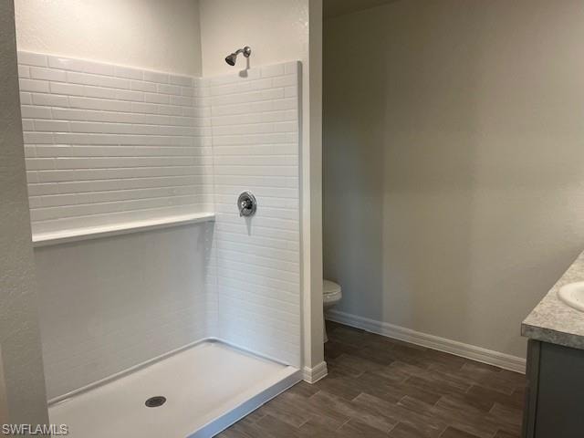 Full bathroom featuring vanity, wood finish floors, tiled shower, and a textured wall