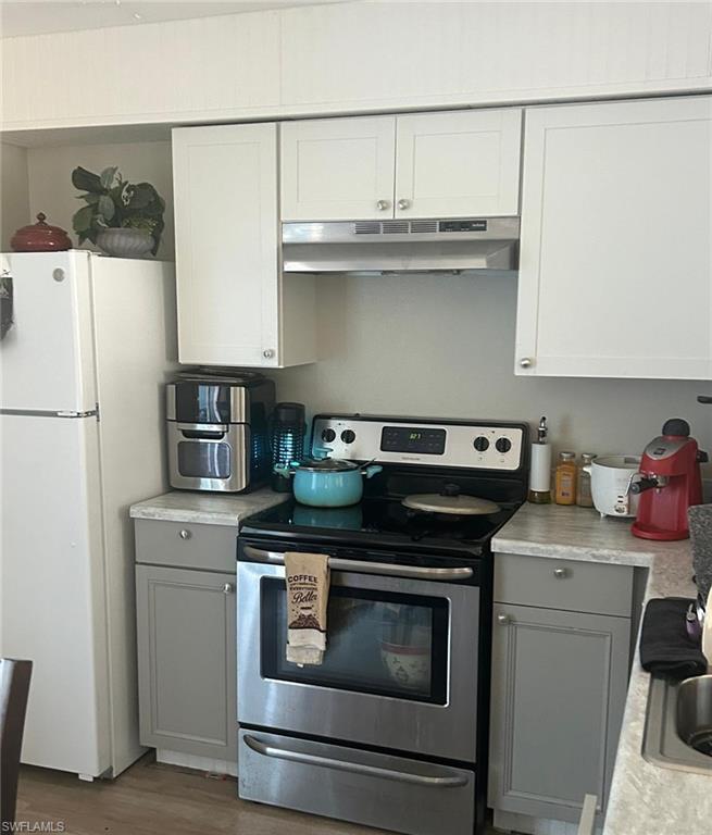 Kitchen with gray cabinetry, under cabinet range hood, light countertops, freestanding refrigerator, and stainless steel range with electric stovetop