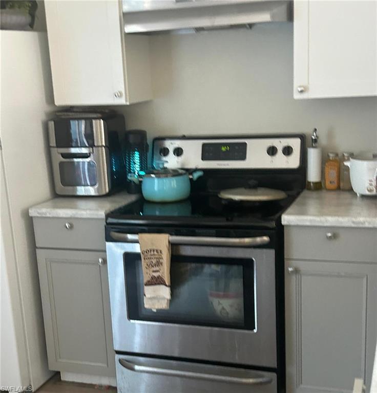 Kitchen featuring electric range, freestanding refrigerator, gray cabinets, light countertops, and exhaust hood