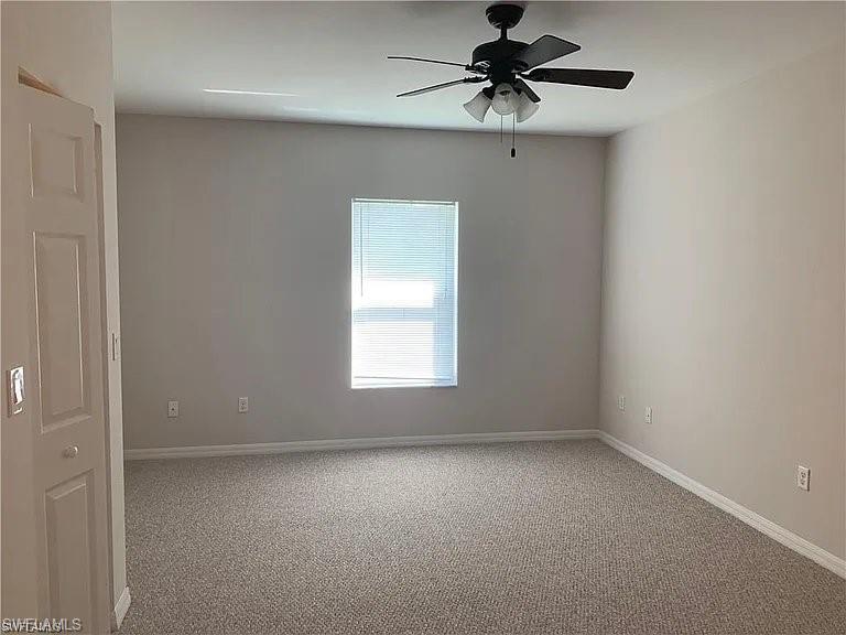 Carpeted empty room featuring a ceiling fan and baseboards