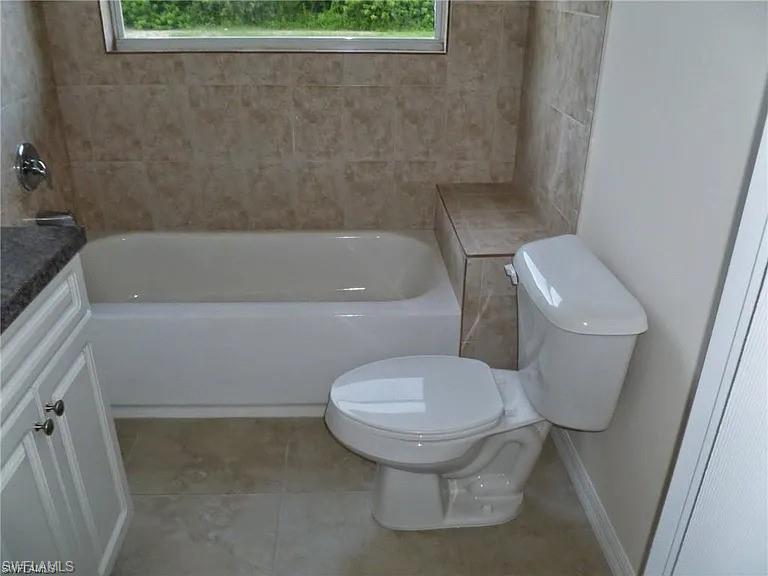 Bathroom featuring tile patterned flooring, a healthy amount of sunlight, toilet, and a tub to relax in