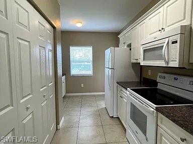Kitchen with baseboards, white appliances, and white cabinets