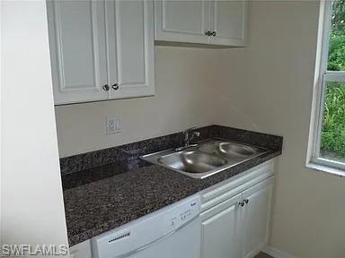 Kitchen featuring a sink, baseboards, white dishwasher, and white cabinetry