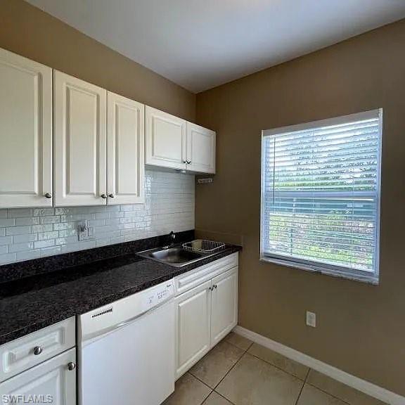 Kitchen featuring light tile patterned floors, white dishwasher, a sink, white cabinetry, and backsplash