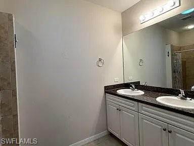 Full bath featuring a sink, baseboards, double vanity, and a tile shower