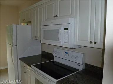 Kitchen featuring white appliances, white cabinets, and dark countertops