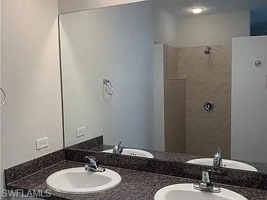 Full bath with a sink, double vanity, and a tile shower
