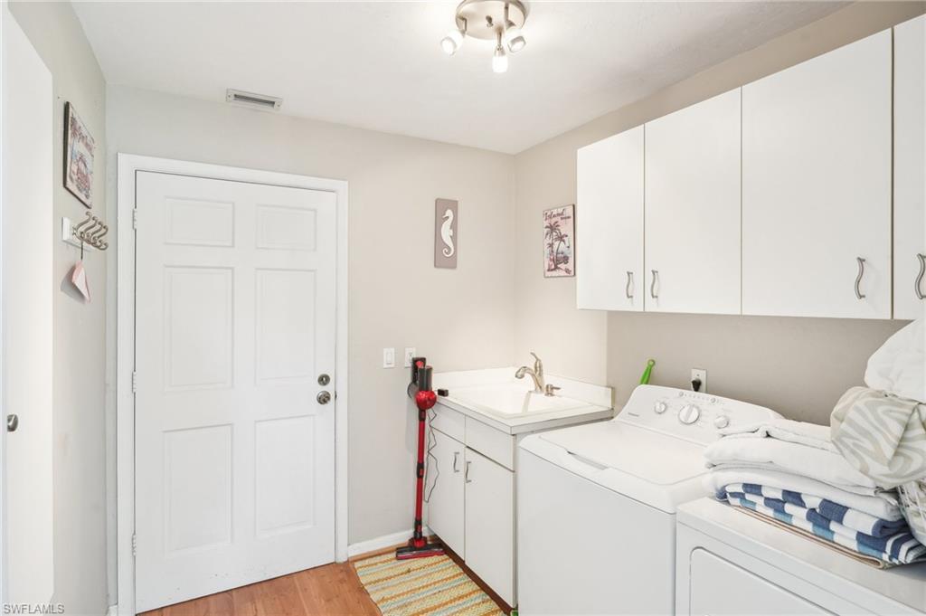 Laundry room with a sink, visible vents, washer and dryer, light wood-type flooring, and cabinet space