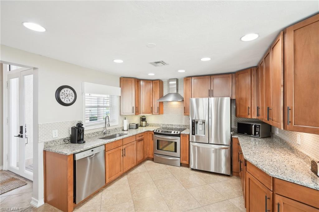 Kitchen with visible vents, appliances with stainless steel finishes, a sink, light stone countertops, and wall chimney exhaust hood