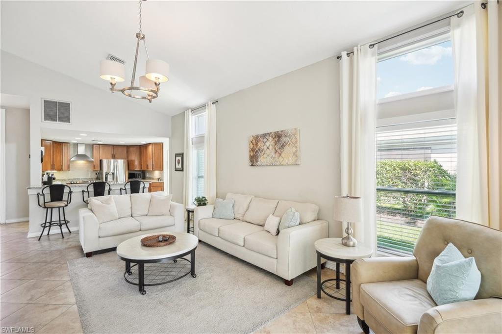 Living area with high vaulted ceiling, light tile patterned flooring, visible vents, and a notable chandelier