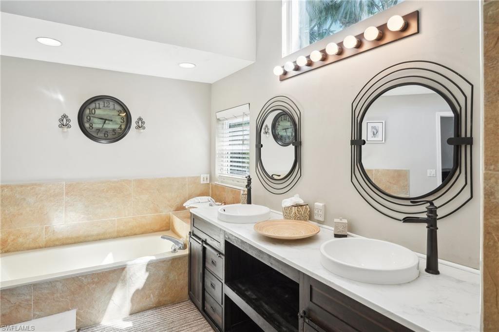 Bathroom featuring a bath, double vanity, a sink, and recessed lighting