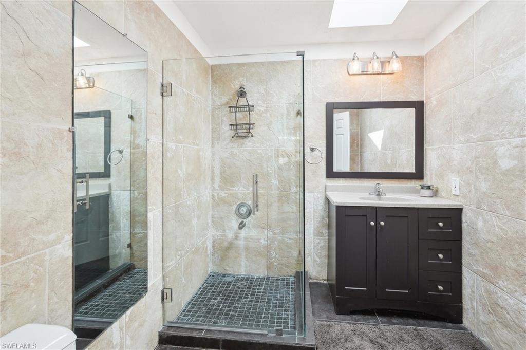Full bathroom with a skylight, tile walls, toilet, a stall shower, and vanity