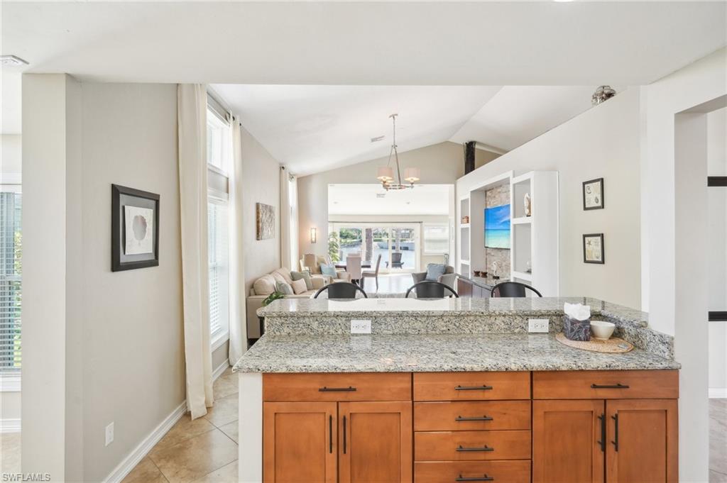 Kitchen featuring brown cabinets, open floor plan, light tile patterned flooring, vaulted ceiling, and light stone countertops