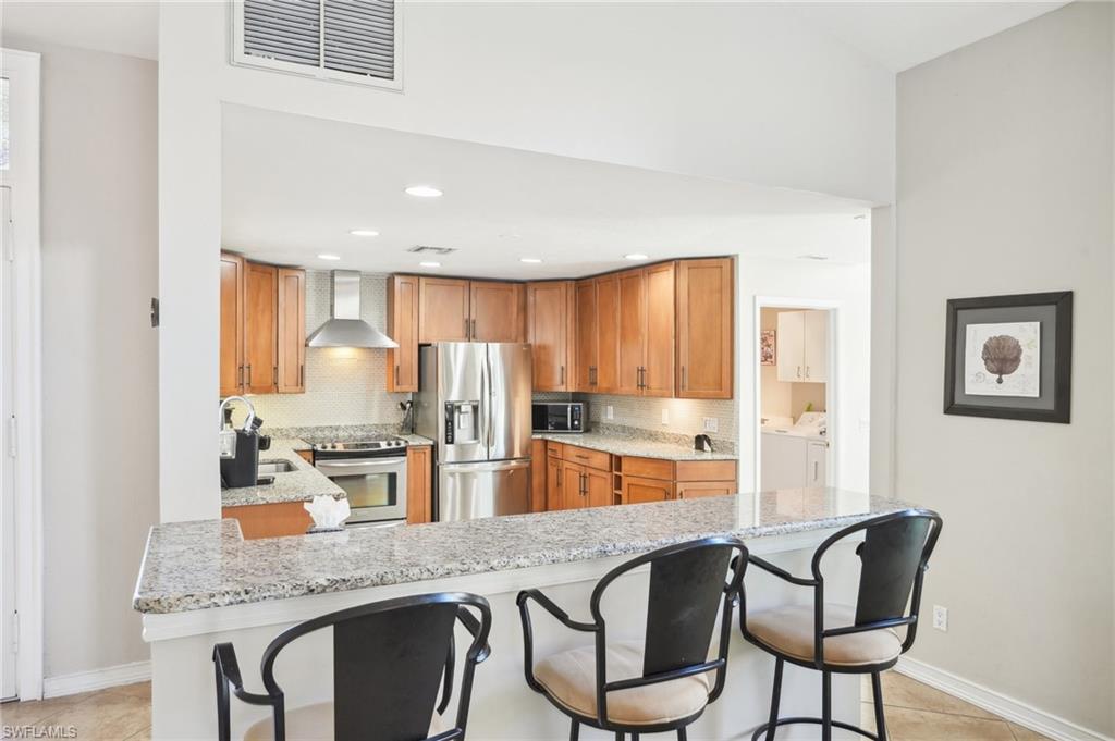Kitchen featuring visible vents, appliances with stainless steel finishes, wall chimney range hood, separate washer and dryer, and a sink
