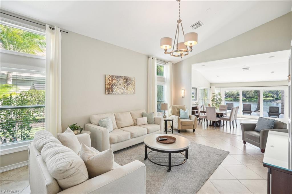 Living room featuring lofted ceiling, light tile patterned flooring, visible vents, plenty of natural light, and an inviting chandelier