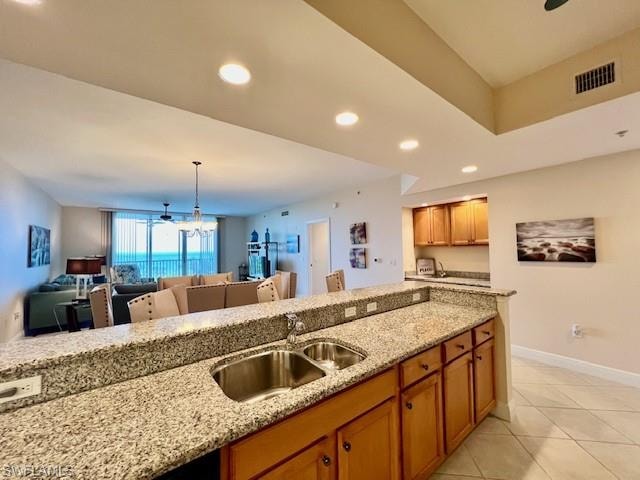 Kitchen featuring a sink, light stone counters, open floor plan, and brown cabinetry