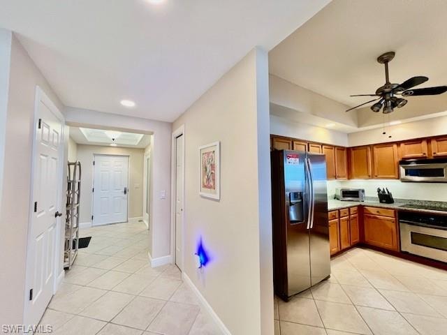 Kitchen with ceiling fan, baseboards, appliances with stainless steel finishes, light tile patterned flooring, and brown cabinetry