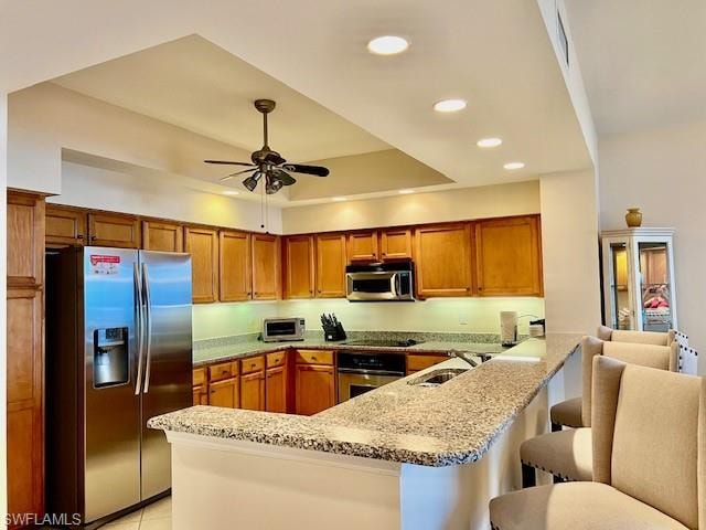 Kitchen featuring ceiling fan, brown cabinets, appliances with stainless steel finishes, a peninsula, and a sink