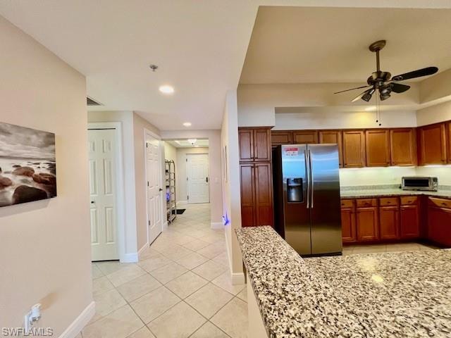 Kitchen with brown cabinetry, stainless steel fridge with ice dispenser, light tile patterned floors, baseboards, and ceiling fan