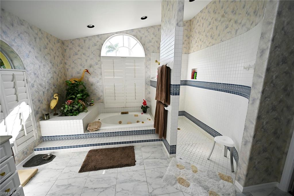 Bathroom with a tub with jets, marble finish floor, a walk in shower, and dual sinks.