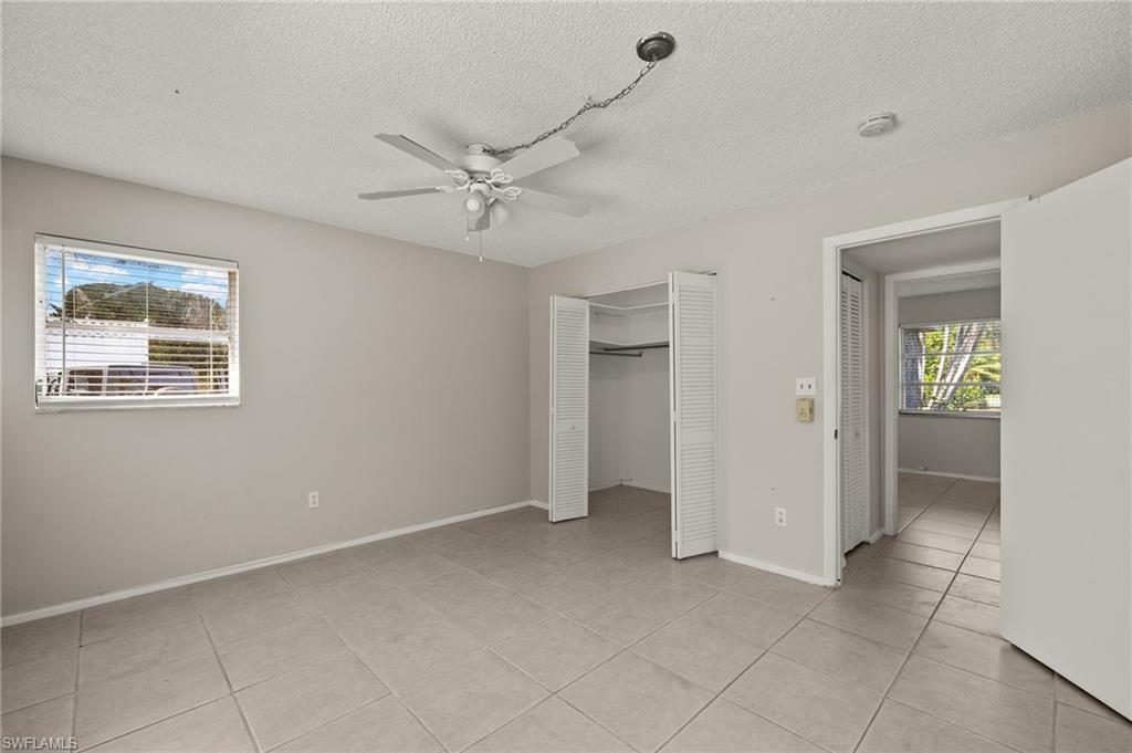 Unfurnished bedroom with a ceiling fan, a textured ceiling, a closet, light tile patterned flooring, and baseboards