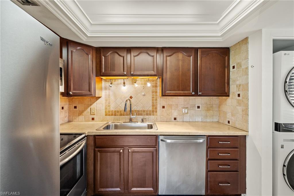 Kitchen featuring crown molding, stacked washer and clothes dryer, appliances with stainless steel finishes, and a sink