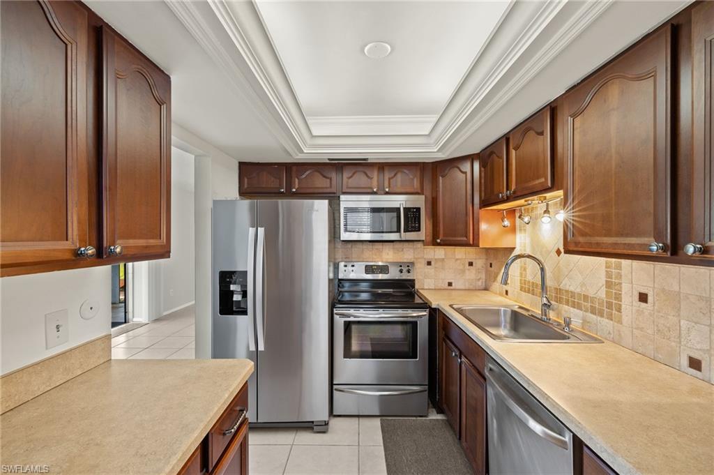 Kitchen with a sink, a tray ceiling, appliances with stainless steel finishes, light countertops, and light tile patterned floors