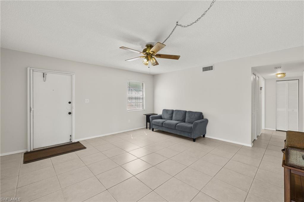 Living area featuring visible vents, a ceiling fan, a textured ceiling, light tile patterned flooring, and baseboards