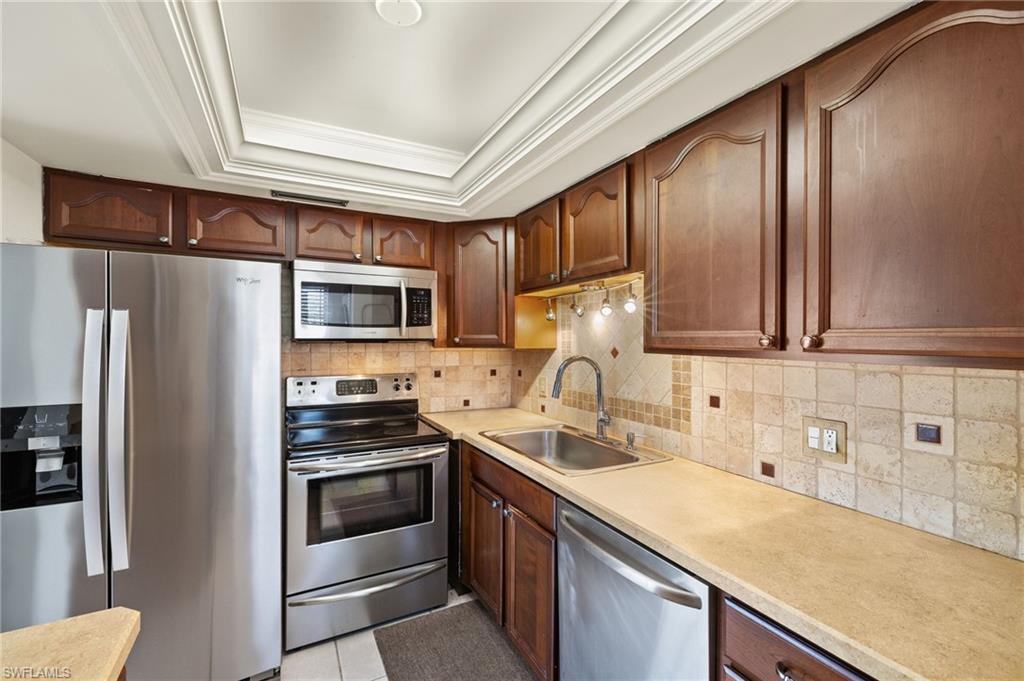 Kitchen with a tray ceiling, a sink, stainless steel appliances, crown molding, and backsplash