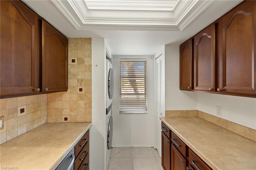 Kitchen with backsplash, light countertops, a tray ceiling, light tile patterned floors, and stacked washer / drying machine