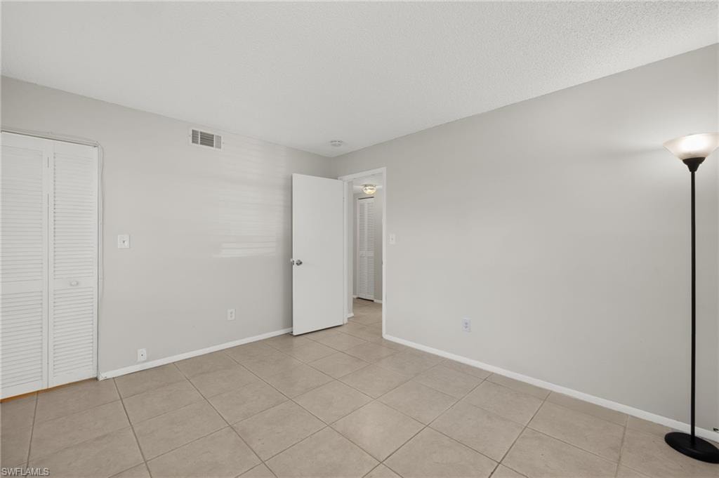 Unfurnished bedroom with light tile patterned floors, visible vents, baseboards, and a textured ceiling
