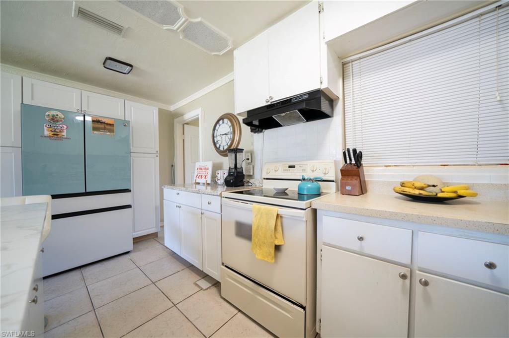 Kitchen with visible vents, under cabinet range hood, light tile patterned floors, freestanding refrigerator, and white electric range oven