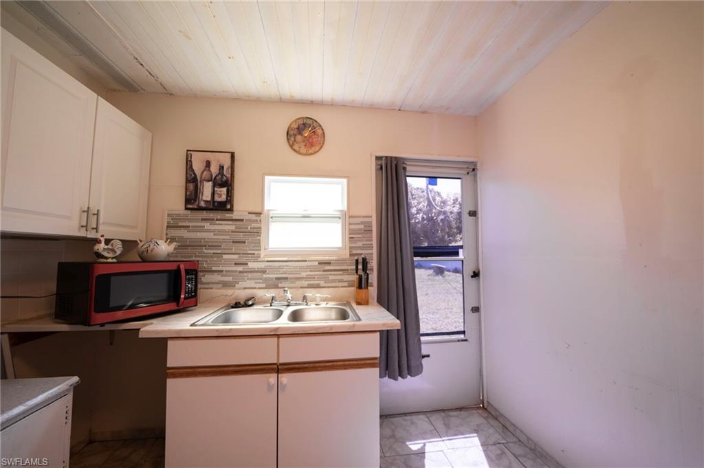Kitchen with a sink, white cabinetry, light countertops, decorative backsplash, and wood ceiling
