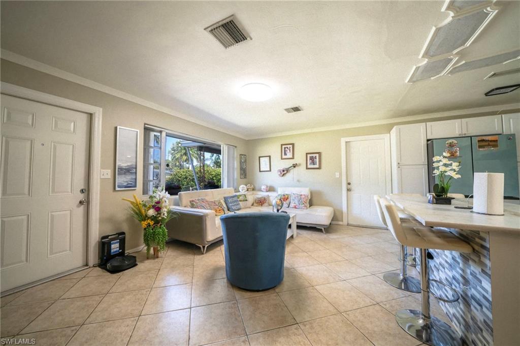 Living area featuring light tile patterned floors, visible vents, and crown molding