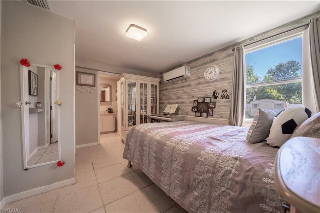 Bedroom featuring a wall mounted air conditioner, visible vents, wooden walls, light tile patterned flooring, and baseboards
