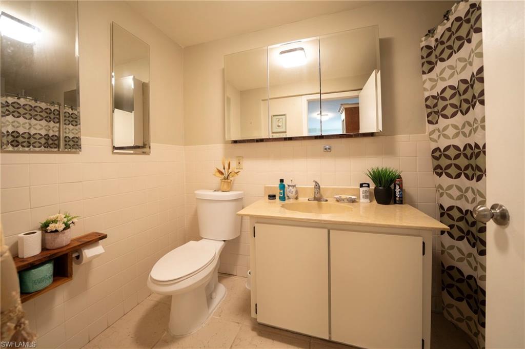 Full bathroom featuring tile walls, wainscoting, toilet, and vanity
