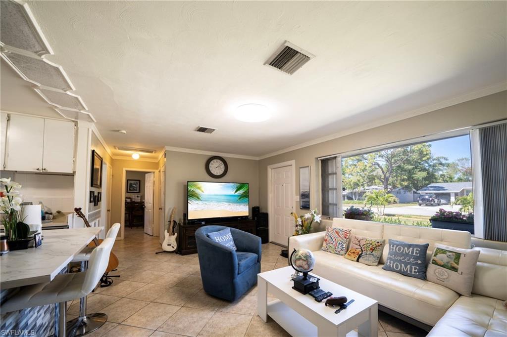 Living area with light tile patterned flooring, visible vents, and crown molding