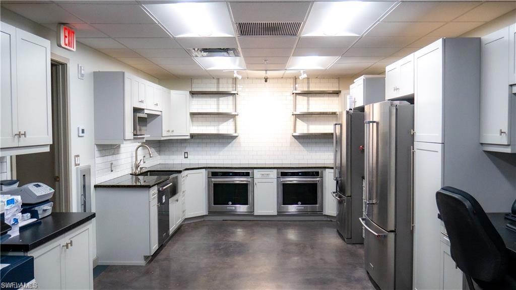 Kitchen featuring dark countertops, a sink, appliances with stainless steel finishes, and open shelves