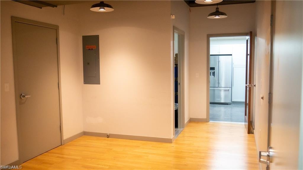 Hallway featuring electric panel, light wood finished floors, and baseboards
