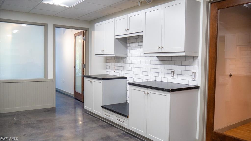 Kitchen featuring decorative backsplash, dark countertops, concrete flooring, and white cabinets