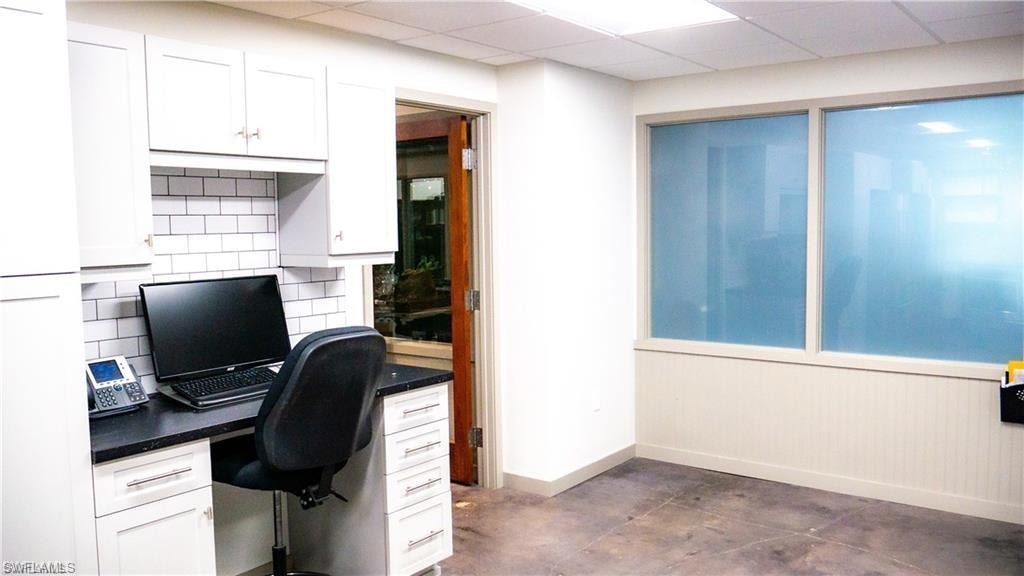 Office featuring a paneled ceiling, baseboards, concrete flooring, and built in desk
