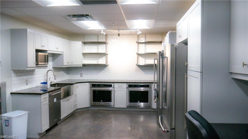 Kitchen with open shelves, a drop ceiling, a sink, appliances with stainless steel finishes, and backsplash